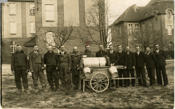 Fotografia grupy pożarników przy dwukołowym, blaszanym wozie